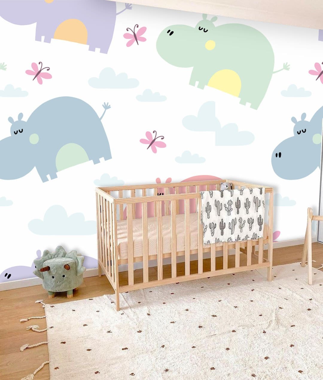 Pastel hippo and butterfly wallpaper in nursery room with wooden crib, rug, and playful decor elements.