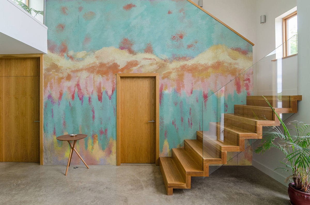 Abstract Pastel Landscape Mural Wallpaper in hallway, wooden stairs, glass railing, concrete flooring, modern decor.