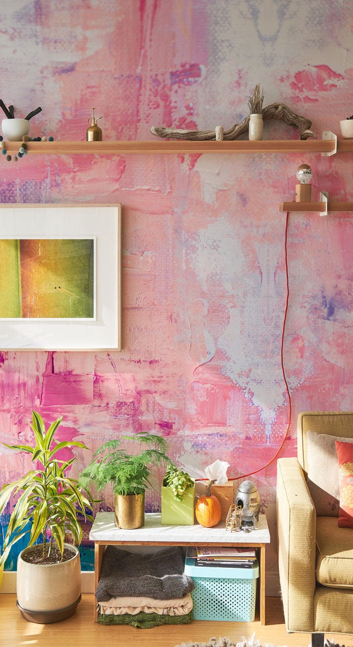 Abstract pastel brushstroke mural wallpaper with pink and peach tones, beige sofa, wooden flooring.