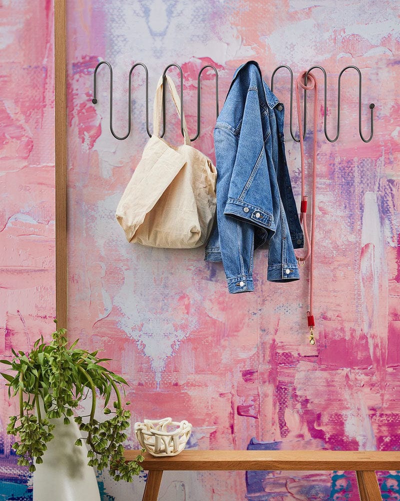 Pink abstract pastel mural wallpaper with wall hooks and clothing, wooden bench, artistic interior design.