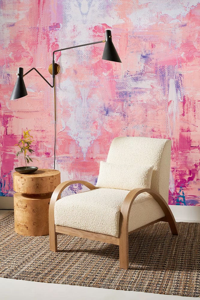 Abstract pastel mural in pink, peach. Armchair, wicker rug, side table, and black wall lamp.