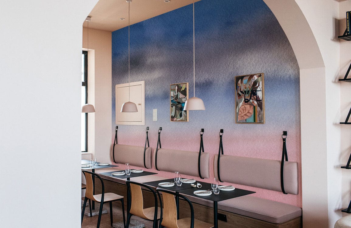 Pastel pink and blue watercolour mural wallpaper, beige dining bench, modern chairs, stylish dining area.