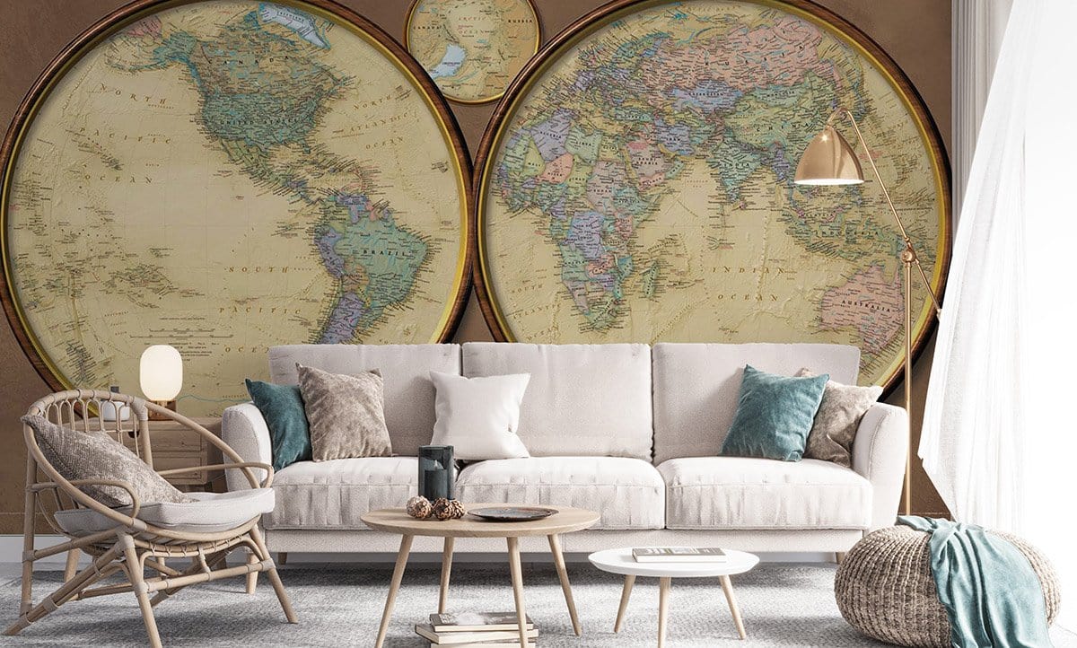 Vintage world map mural wallpaper with earth tones in a living room; neutral sofa, rattan chair.