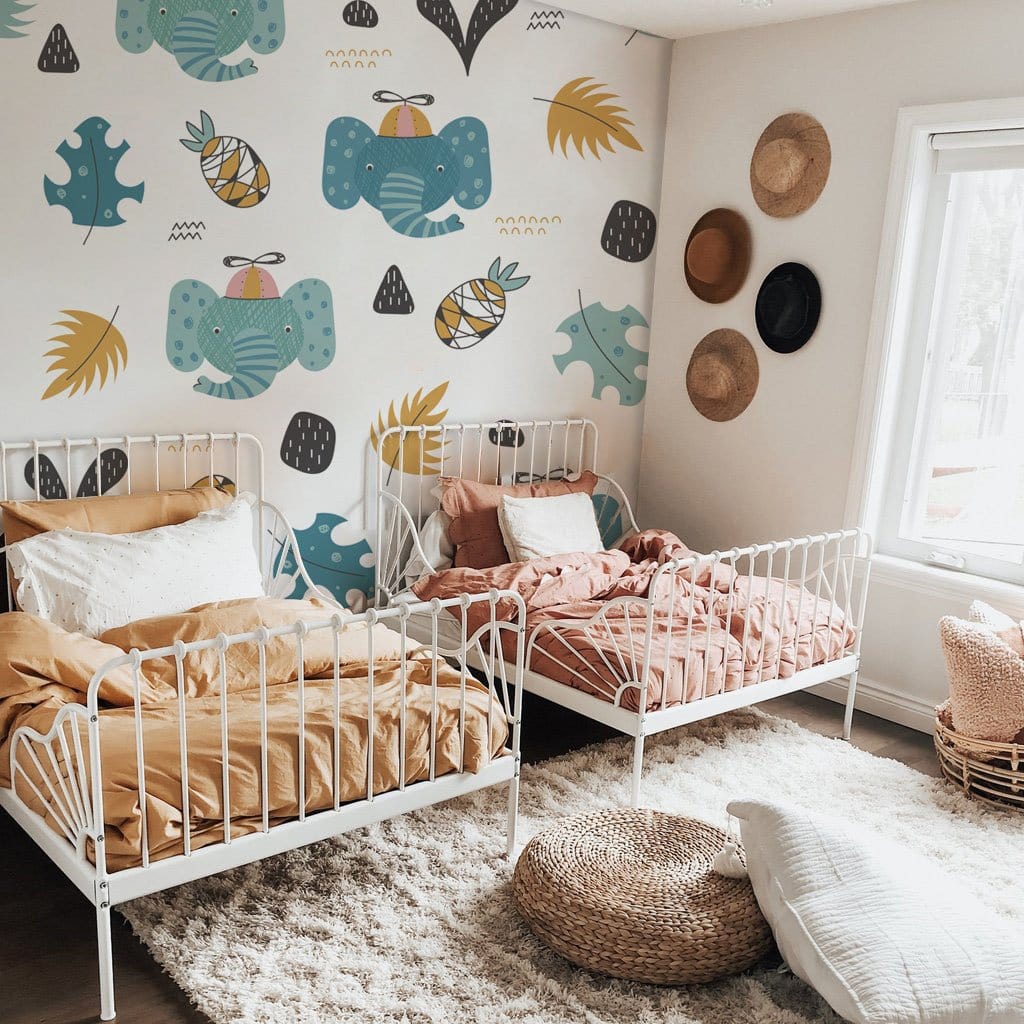 Children's room with Whimsical Elephant Jungle mural, white metal beds, beige rug, and woven wall hats.