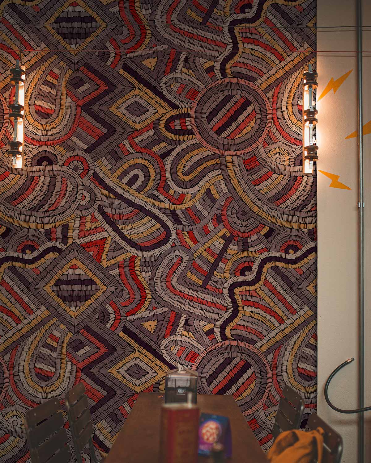 Multicoloured geometric mosaic pattern wallpaper with vibrant tribal design, dining room, wooden table, chairs.