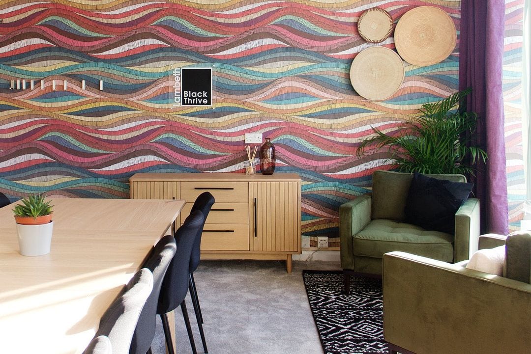 Colourful geometric wave wallpaper, wooden sideboard, green armchair, grey carpet, dining chairs, wall decor.