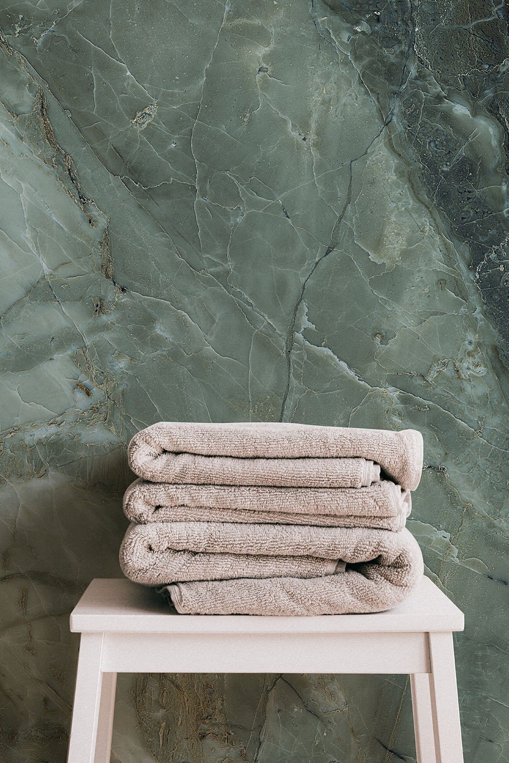 Emerald Onyx Marble Effect Wallpaper with luxurious green texture, stool with stacked towels.