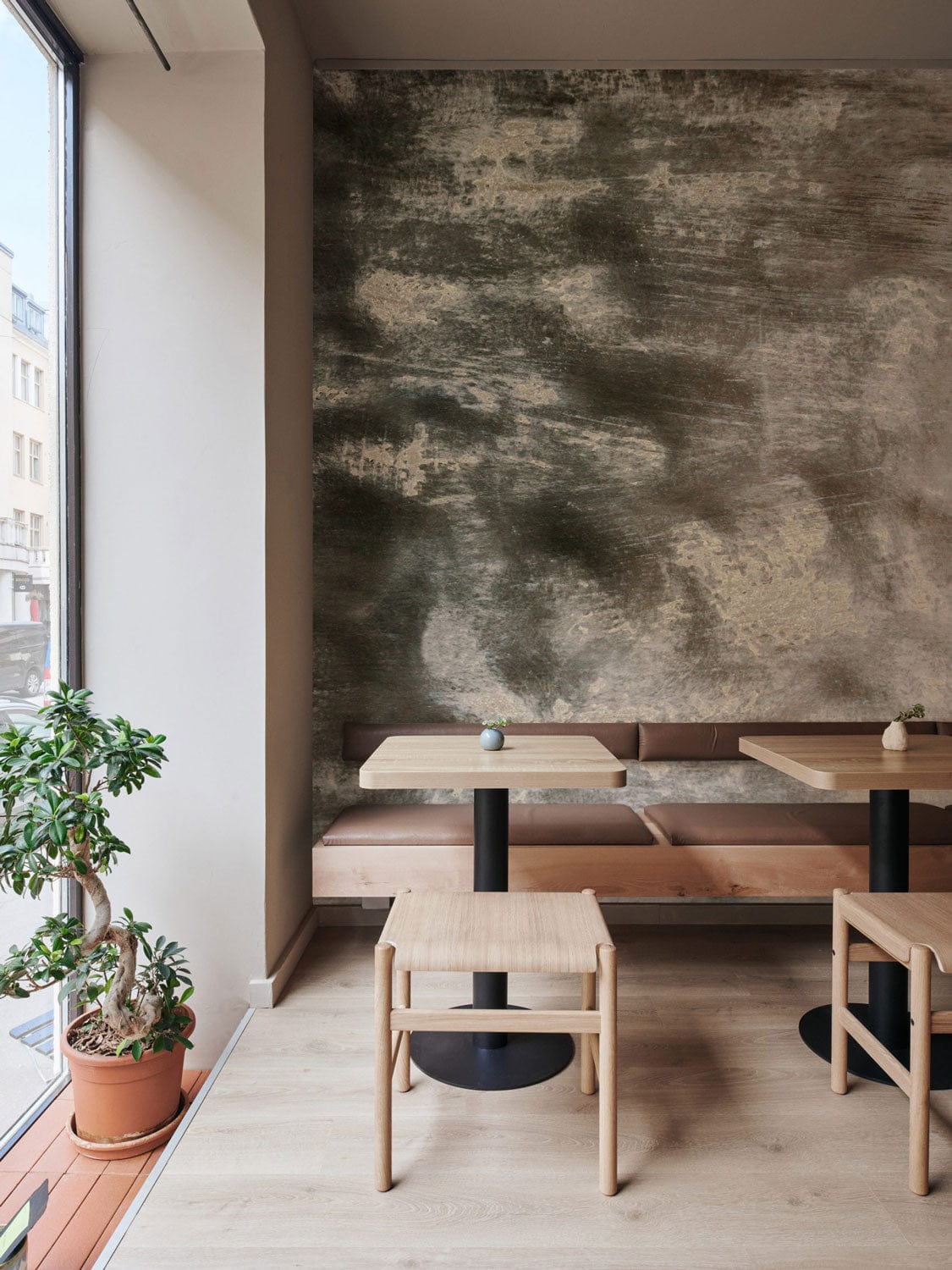 Contemporary cafe with Abstract Misty Grey Textured Mural Wallpaper, wooden tables, beige bench seating, light flooring.