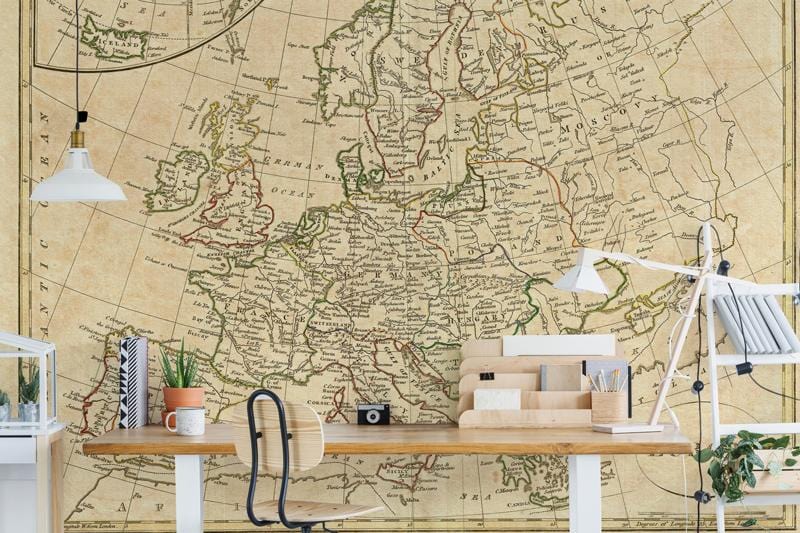 Vintage European map mural wallpaper in study room with wooden desk, black chair, and white lamps.