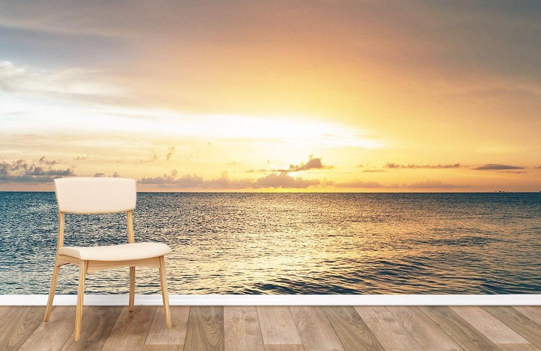 Golden Horizon Ocean Sunset Mural Wallpaper with beige chair, wood flooring, serene coastal landscape decor.