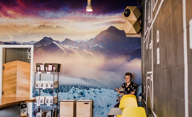 Majestic Mountain Sunrise Wallpaper, vibrant winter hues, modern café setting with yellow chairs, wooden flooring.