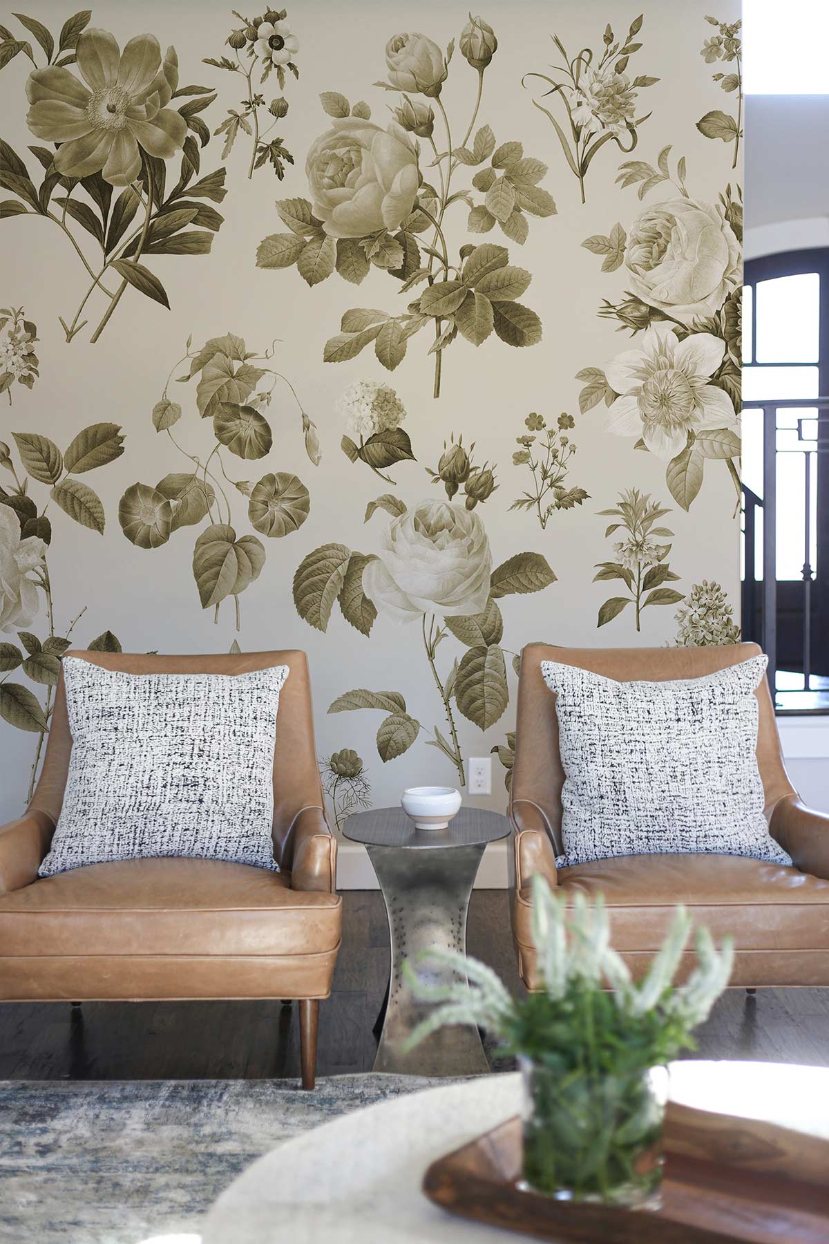 Vintage sepia floral botanical wallpaper in living room with tan leather chairs and rustic side table.