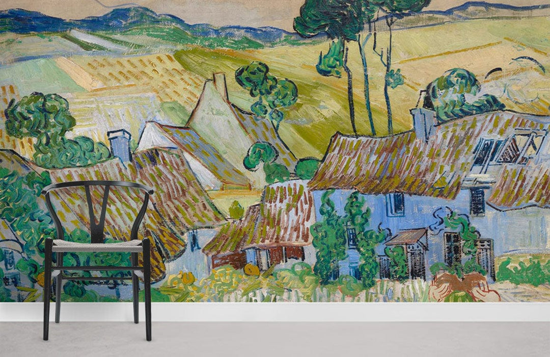 Charming mural wallpaper featuring rustic cottages, vibrant blues and greens, with modern chair on grey floor.