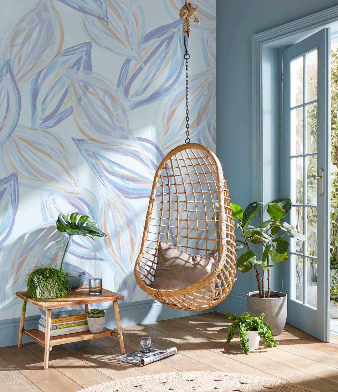 Elegant pastel leaf wallpaper, blue walls, rattan hanging chair, wooden floor, serene room decor.