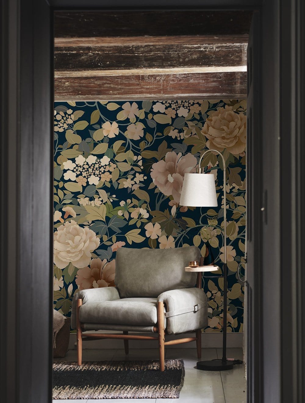 Elegant navy floral mural wallpaper with pastel blooms, grey armchair, wooden beams, stylish floor lamp.