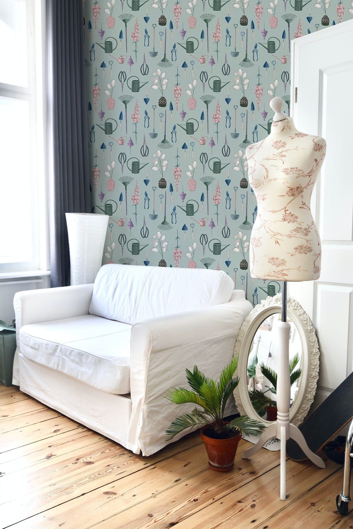 Whimsical wallpaper in soft teal with white sofa, mannequin, and wooden flooring in stylish room.