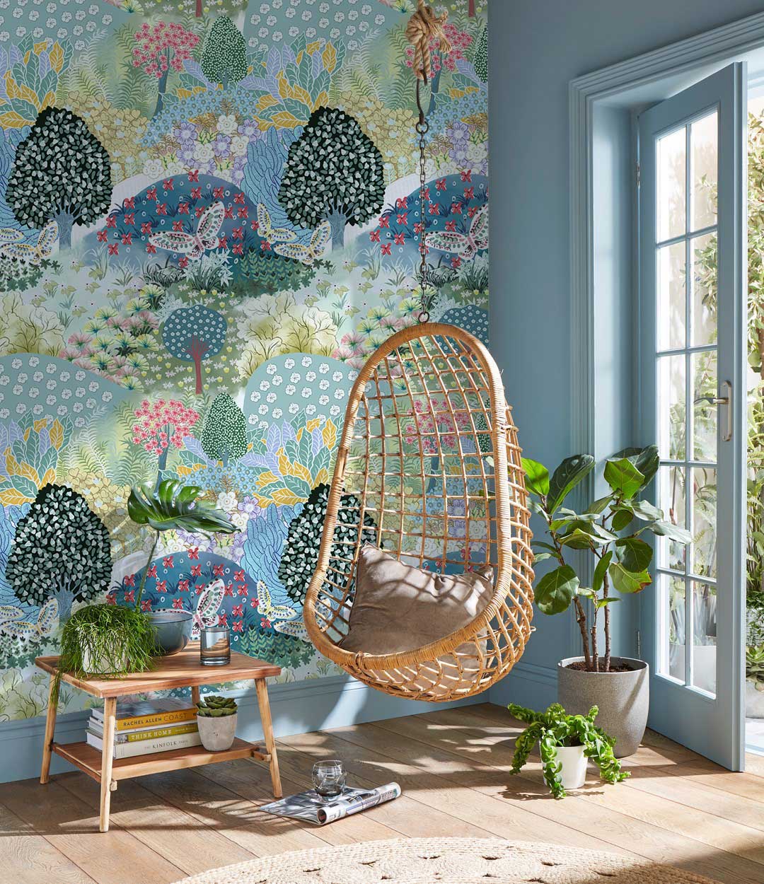 Vibrant pastel woodland wallpaper, wicker chair, light blue walls, wooden flooring, contemporary living room decor.