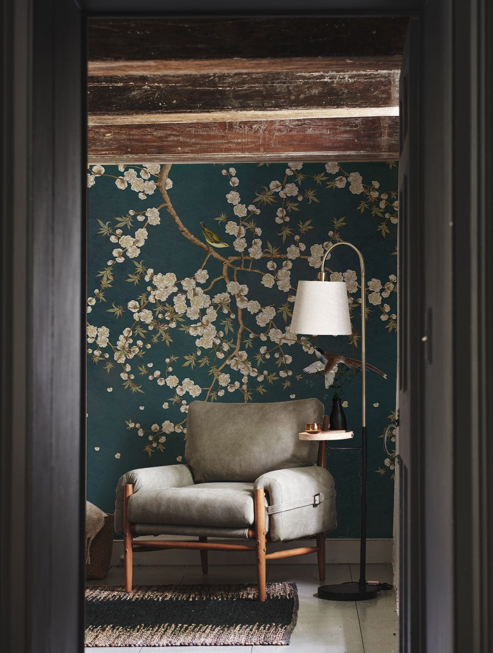 Elegant teal blossom branches wallpaper mural with grey armchair, wooden beams, and floor lamp in room.