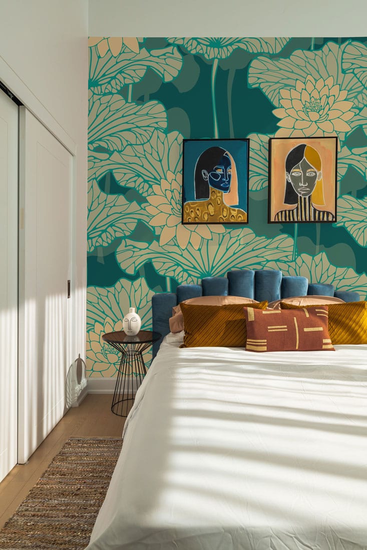 Teal and cream floral lotus wallpaper in bedroom with art, blue headboard, and white bedding.