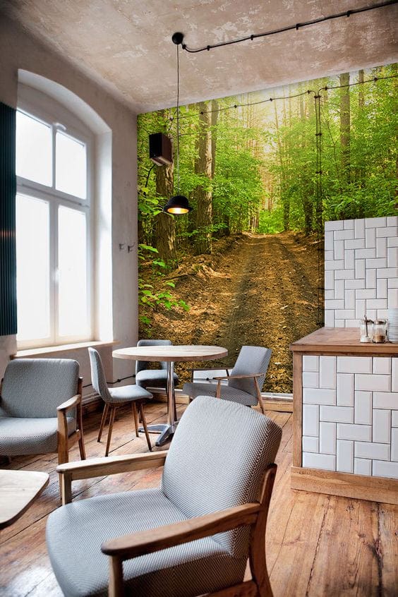 Sunlit Forest Path Mural Wallpaper in modern dining room, featuring wooden flooring and grey armchairs.