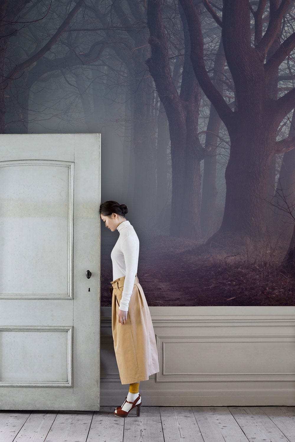 Misty Enchanted Forest Mural Wallpaper in misty grey; white door; wooden flooring; living room setting.