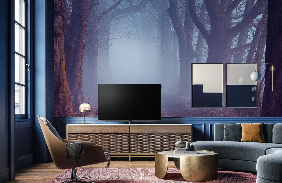 Misty Enchanted Forest Mural Wallpaper in moody grey living room with blue sofa and wood flooring.