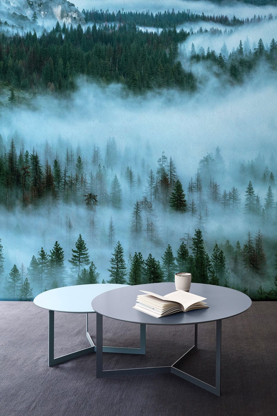 Misty Forest landscape mural wallpaper, serene green tones, grey tables on dark flooring, tranquil room.