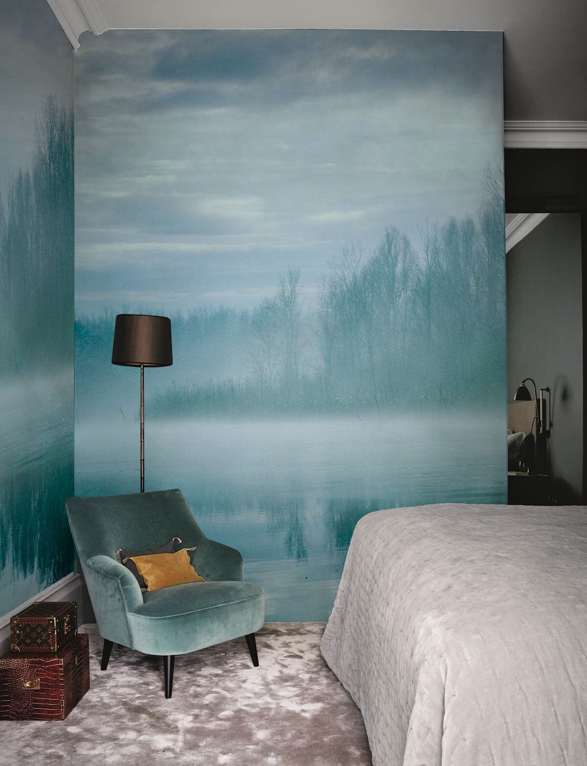 Misty Teal Forest River Mural Wallpaper in bedroom with teal armchair, grey bed, and carpet flooring.