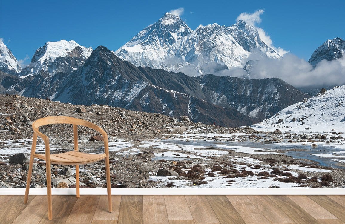 Majestic Snowy Mountain Mural in earthy tones, wooden flooring, minimalist chair, blue sky backdrop.