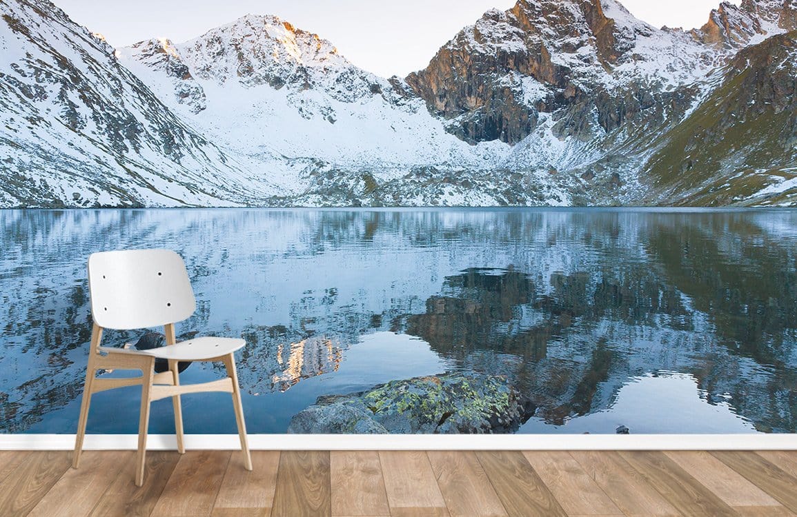 Scenic Alpine lake and mountain wallpaper with modern chair, wood flooring; serene blue wall mural.
