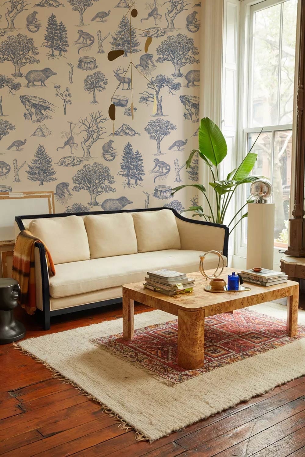 Vintage forest wallpaper in living room with beige sofa, wooden flooring, elegant design.