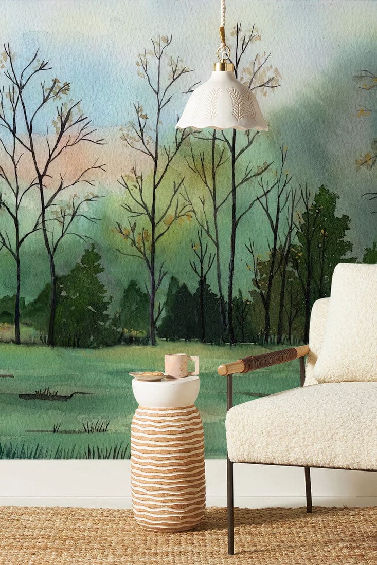 Cozy room with woodland mural wallpaper, textured rug, cream sofa, pendant light, and wooden handle chair.