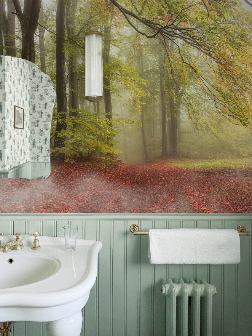 Misty Autumn Forest Mural Wallpaper in bathroom with green panelling, white sink, and towel rail.