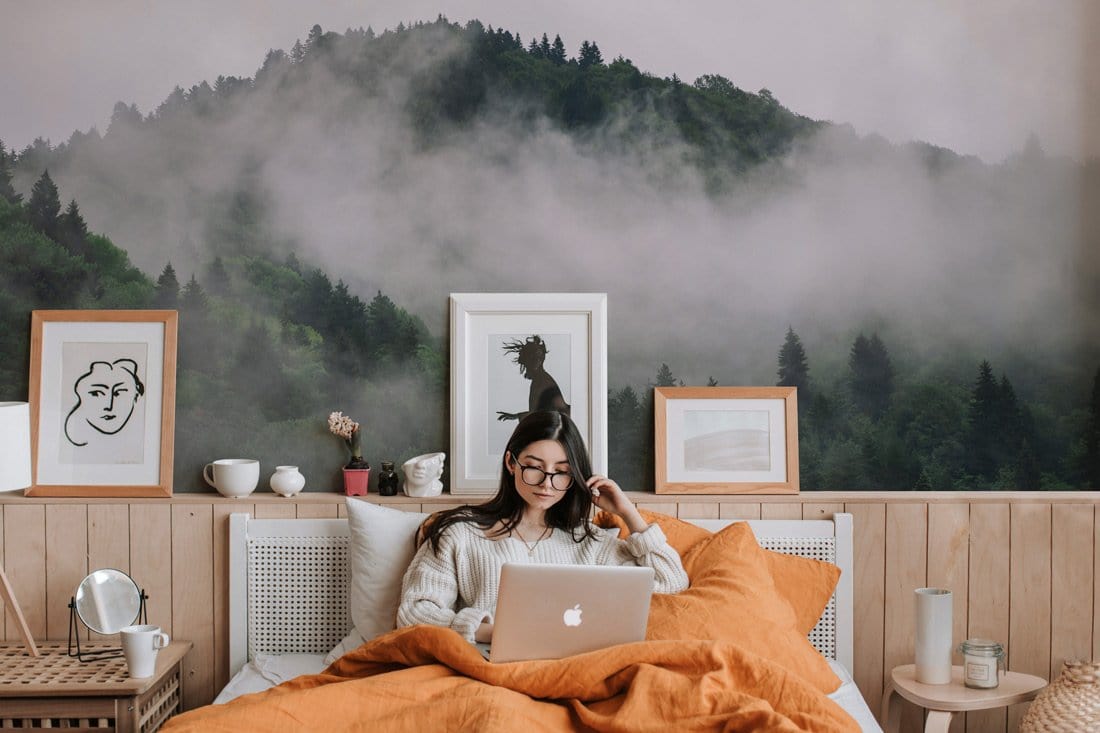 Enchanted Misty Forest Green Wallpaper in cosy bedroom with orange bedding and wooden wall accents.
