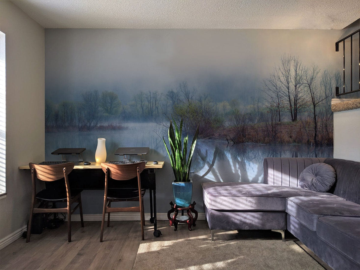 Misty Blue Tranquil Lakeside Mural Wallpaper in lounge with grey sofa, wooden chairs, laminate flooring.