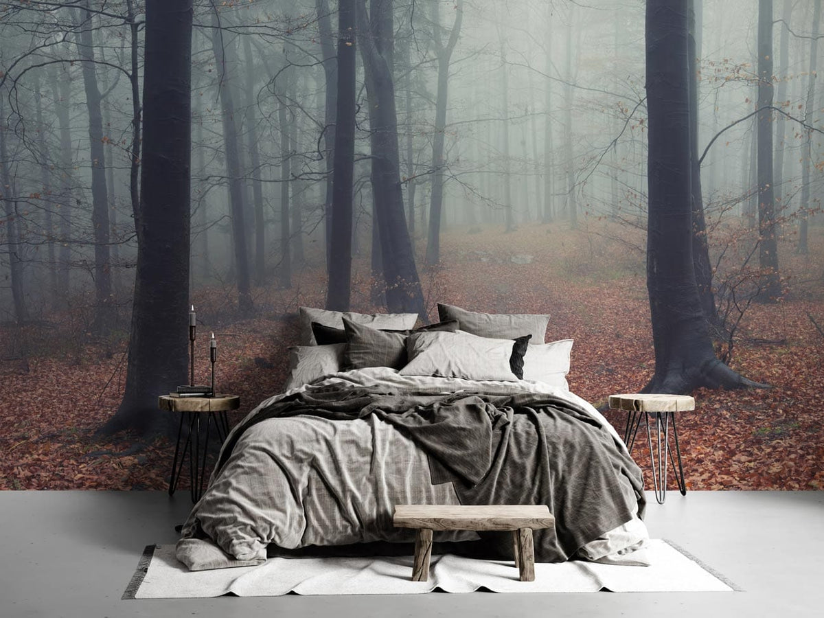 Misty forest mural wallpaper in bedroom; grey bedding, rustic tables, wood bench, light flooring.