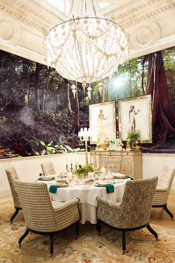 Dining room with sunlit forest mural wallpaper, elegant chandelier, patterned chairs, and classic furniture.