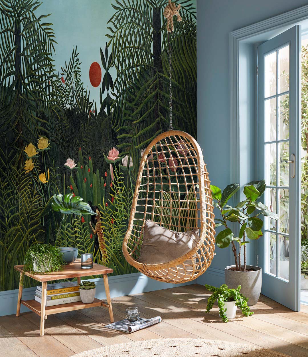 Vintage Jungle Mural Wallpaper in living room with rattan swing chair, light wood flooring, and blue walls.