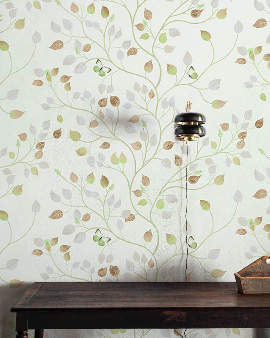 Elegant Leafy Branches Wallpaper in soft green, wooden table, modern lamp, earthy tones motif.