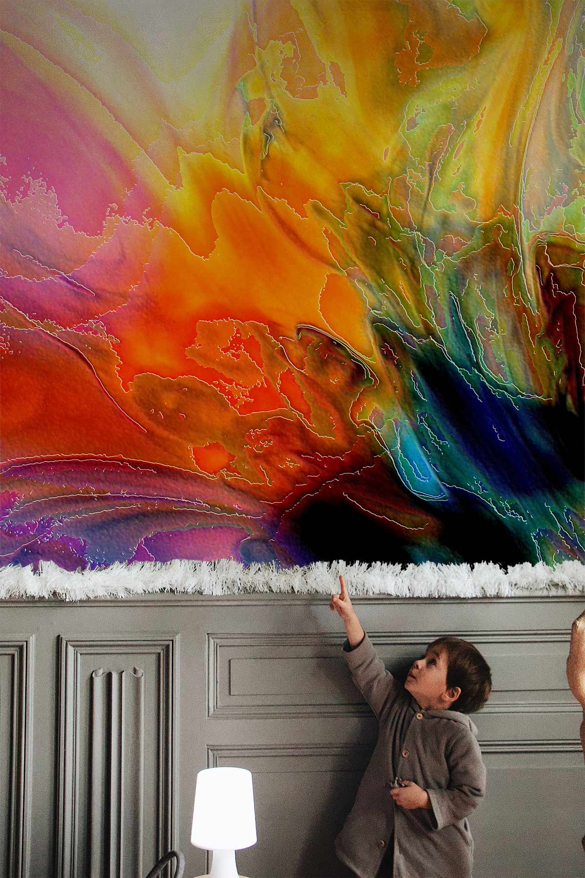 Multicolour abstract mural wallpaper with child pointing, grey panelled wall, modern lamp in living room.