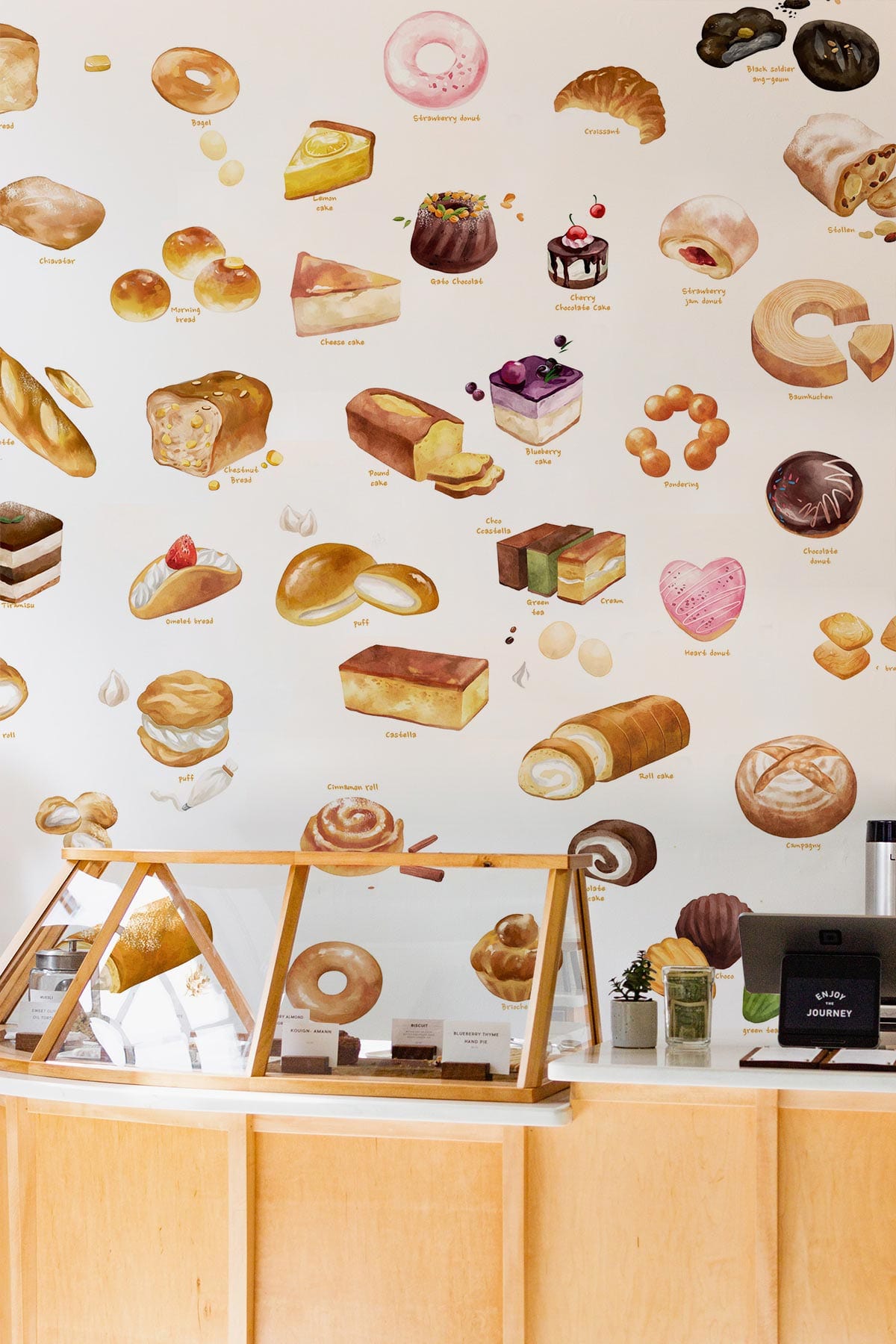 Artisan Bakery Treats Wallpaper in bakery setting with light wooden counter, showcasing colourful pastry designs.