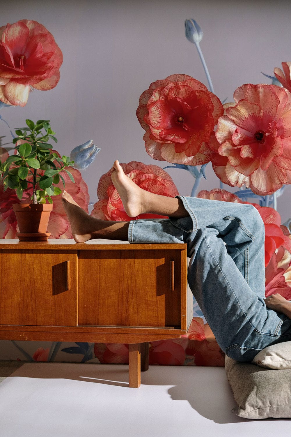 Vintage coral floral mural wallpaper with blue accents, mid-century sideboard, casual blue jeans setting.