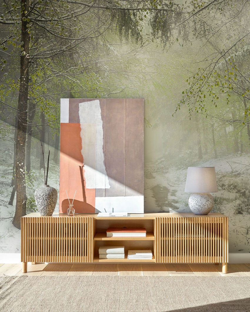 Enchanted Winter Forest mural wallpaper in misty green tones behind wooden sideboard in modern living room.