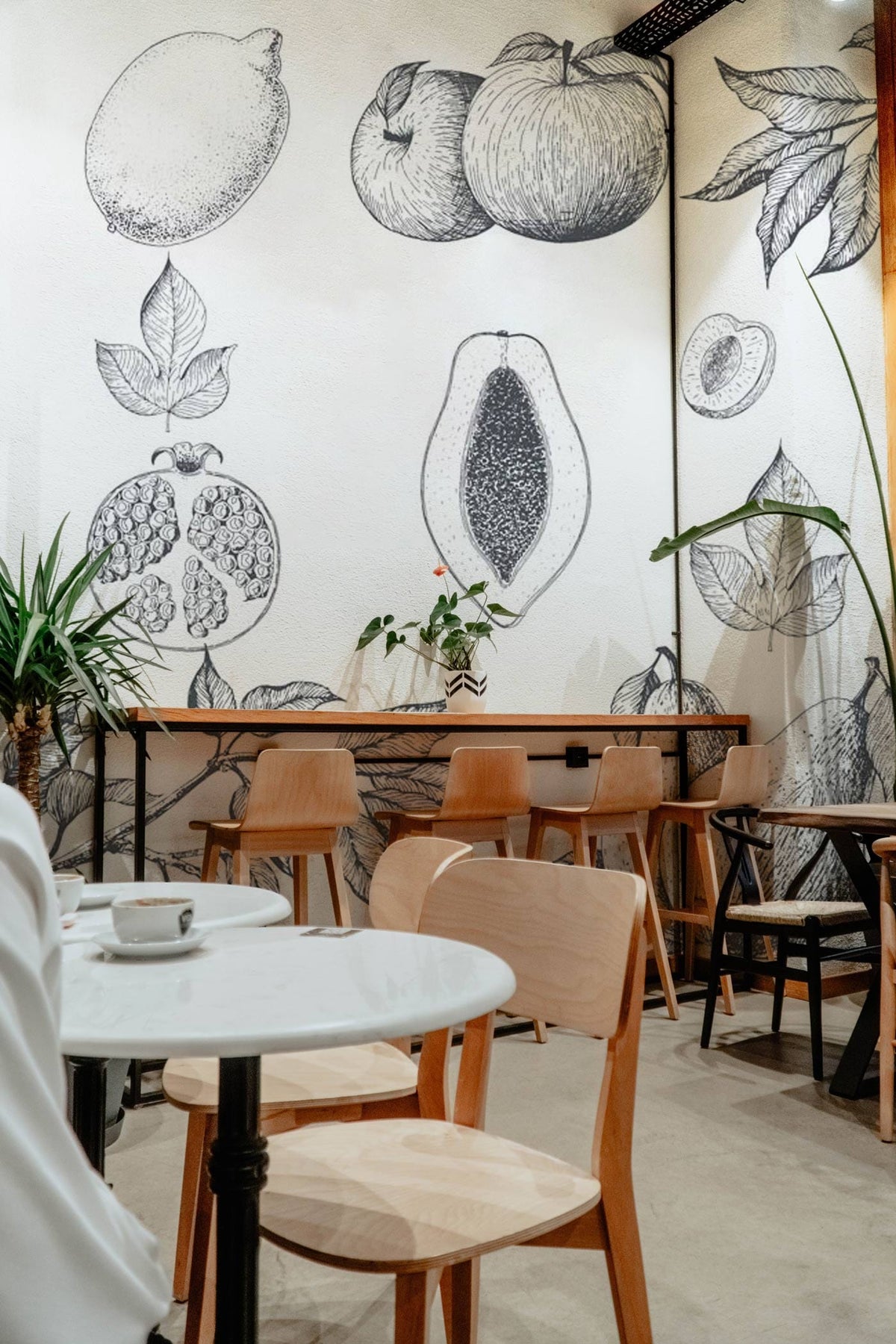 Monochrome botanical fruit sketch wallpaper in elegant café with light wood furniture and minimalist decor.