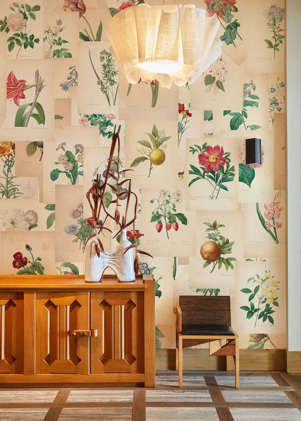 Vintage Botanical Floral Art Print Wallpaper in pastel, with wooden sideboard, chair, and modern light fixture.