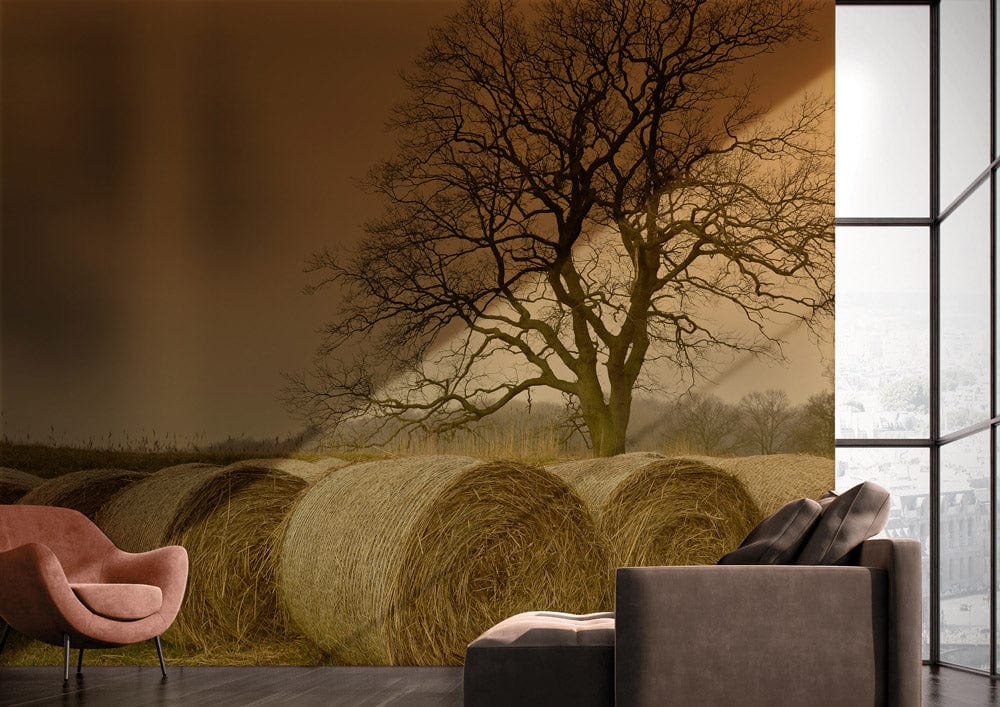 Rustic countryside mural wallpaper with hay bales, tree, pink chair, grey sofa, modern room.