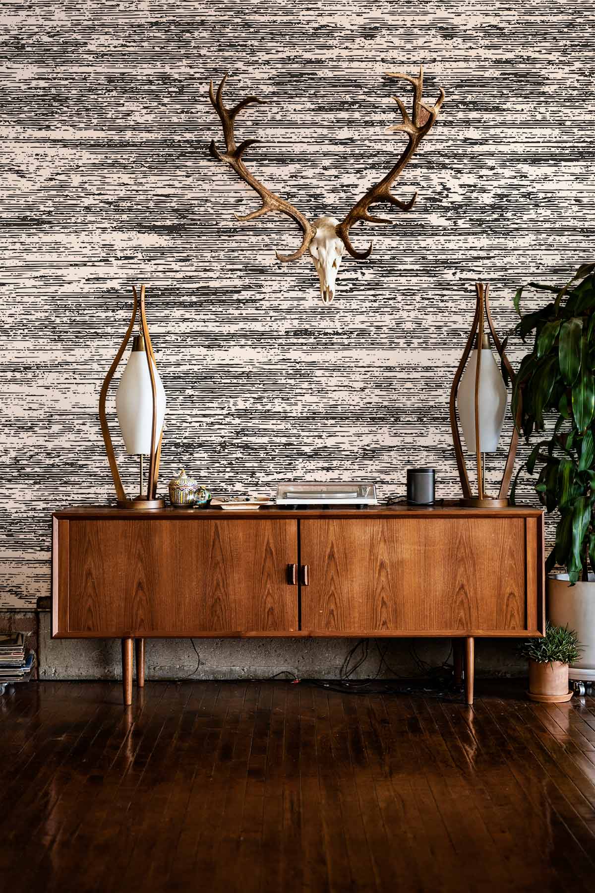 Monochrome Textured Wallpaper behind vintage wooden sideboard with mirrored lamps, hardwood floor, antler decor.