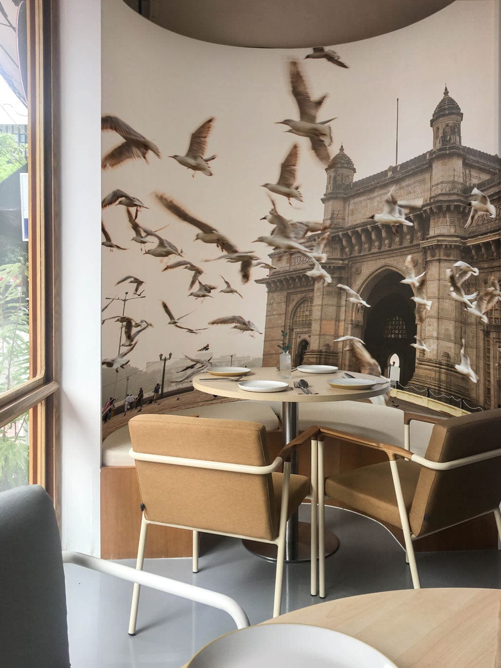 Vintage Gateway of India mural wallpaper in dining room with beige chairs, round table, grey flooring.