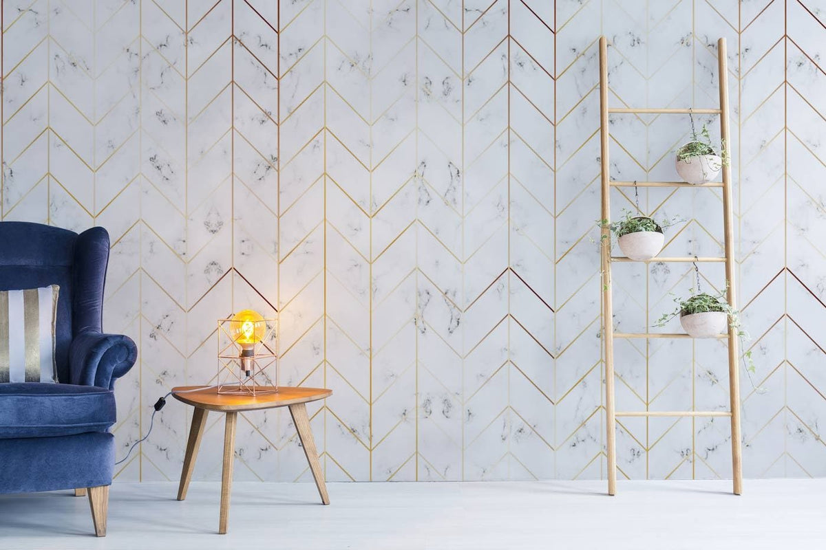 Luxurious white marble chevron wallpaper with gold accents, blue velvet sofa, wooden ladder, side table.