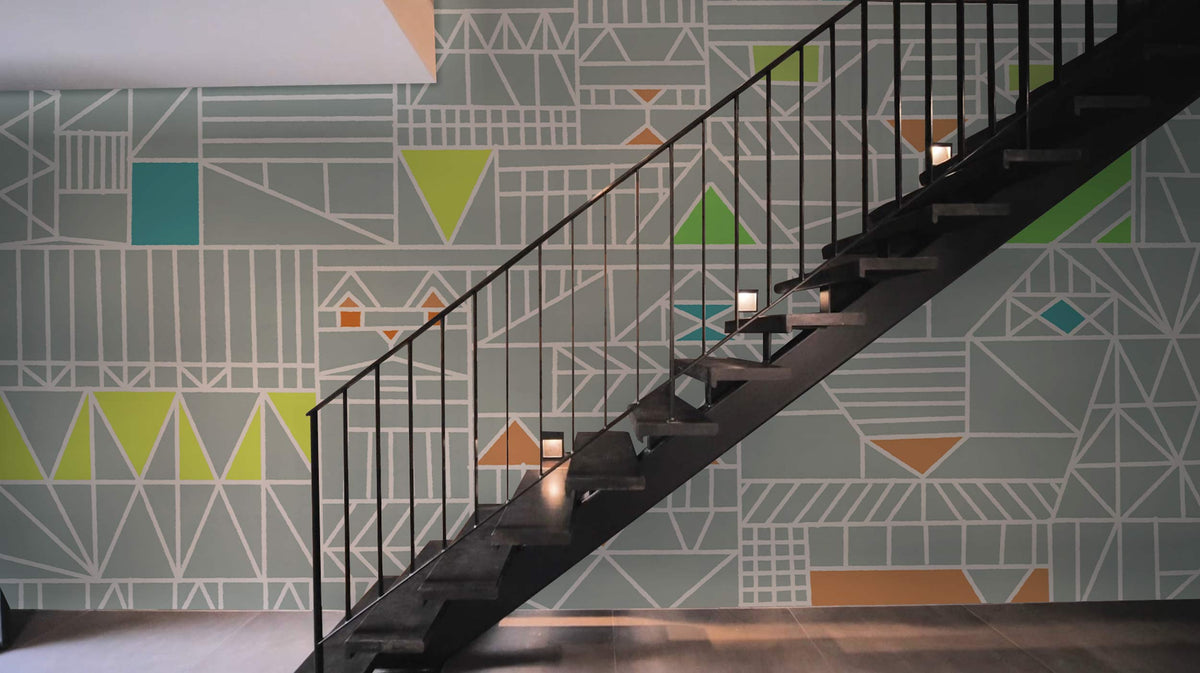 Geometric Abstract Pattern Wallpaper in Soft Grey behind black staircase, modern interior, wooden flooring.